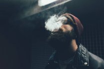 Hipster in knit hat smoking at night — Stock Photo