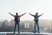 Male hipsters standing on city wall with arms out — Stock Photo