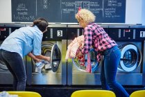 Жінки вставляють білизну в пральні машини — стокове фото