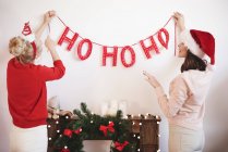 Вид сзади на двух молодых женщин, вешающих рождественские украшения на стену — стоковое фото