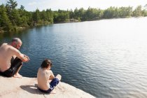 Pai e filho sentados à beira do lago — Fotografia de Stock