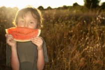 Boy eating watermelon in tall grass — Stock Photo