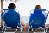 Couple on sun beds holding hands — Stock Photo