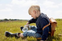 Niño llenando tarro en campo herboso - foto de stock
