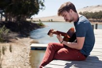 Mann sitzt auf Seebrücke und spielt Gitarre — Stockfoto