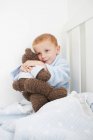 Junge umarmt Teddybär im Bett — Stockfoto