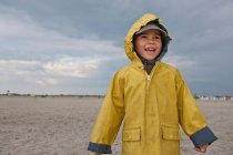 Niño sonriente con impermeable en la playa - foto de stock