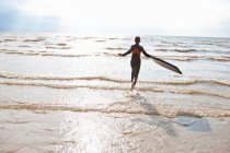 Девушка в гидрокостюме бежит по волнам — стоковое фото