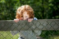 Garçon regardant sur la clôture en bois à l'extérieur — Photo de stock