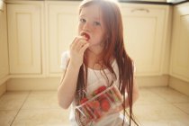 Девушка ест клубнику на полу кухни — стоковое фото