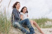 Madre e hija sentadas en la playa - foto de stock