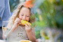 Menina comer milho à mesa ao ar livre — Fotografia de Stock