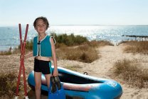 Niño sosteniendo aletas cerca de la canoa en la playa - foto de stock