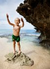 Мальчик стоит на скале на пляже — стоковое фото