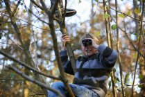 Хлопчик на дереві дивиться через бінокль в лісі восени — стокове фото