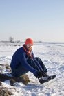 Mann schnürt Schlittschuhe im verschneiten Feld — Stockfoto
