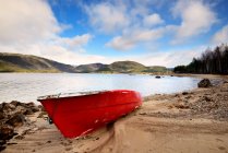 Красная лодка на берегу озера — стоковое фото