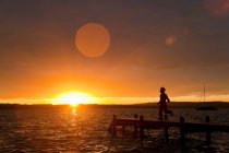 Хлопчик біжить на дерев'яному причалі на заході сонця — стокове фото