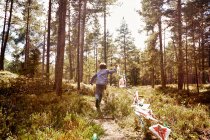 Chico corriendo a través de bosque tirando de bunting - foto de stock