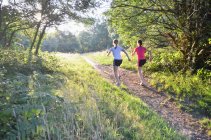 Dos jóvenes corredoras corriendo por la pista forestal por la mañana - foto de stock