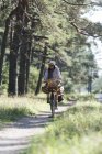 Mulher pedalando no caminho da floresta com cestas de forrageamento — Fotografia de Stock