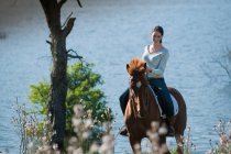 Woman riding horse by rural lake — Stock Photo