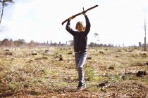 Boy holding up a stick in a plantation clearing — Stock Photo