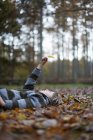 Мальчик лежит на лесной подстилке, держа лист в воздухе. — стоковое фото