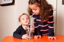 Дівчинка і хлопчик п'ють воду з соломинками — стокове фото