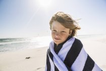 Ragazzo sulla spiaggia avvolto in asciugamano a strisce guardando la fotocamera — Foto stock