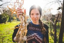 Young woman in garden holding freshly picked garlic bulbs looking at camera smiling — Stock Photo