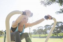 Mitte erwachsene Frau trainiert auf Rudergerät im Park — Stockfoto