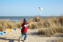 Young boy running towards sea with kite — Stock Photo