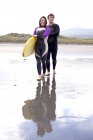 Porträt eines Paares mit Surfbrett am Strand — Stockfoto