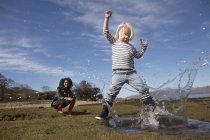 Boy splashing in puddle in meadow at daytime — Stock Photo