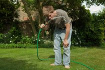 Мальчик пьет воду из шланга на открытом воздухе — стоковое фото