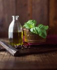 Aceite de oliva virgen extra, albahaca y bayas de enebro sobre tabla de cortar de madera - foto de stock