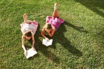 Girls lying on grass reading books — Stock Photo