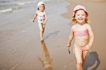Chicas sonrientes caminando en olas en la playa - foto de stock