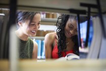 Две молодые студентки колледжа читают книги на библиотечных полках — стоковое фото