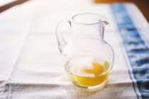 Raw egg in glass jug on table, close up shot — Stock Photo