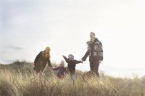 Середня доросла пара, що стоїть у піщаних дюнах зі своїм сином, дочкою та собакою — стокове фото