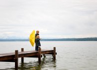Children with yellow umbrella on dock — Stock Photo