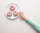 Рука тягнеться до пончиків на тарілці — стокове фото