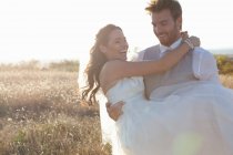 Newlywed groom carrying bride outdoors — Stock Photo
