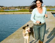 Donna che corre con cane vicino a un lago — Foto stock