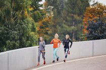 Three female runners running along park road — Stock Photo