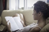 Jeune femme lecture livre sur canapé — Photo de stock