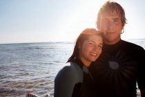 Пара стоящих на пляже с доской для серфинга — стоковое фото