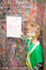 Boy pointing to painting on paint-splattered wall — Stock Photo